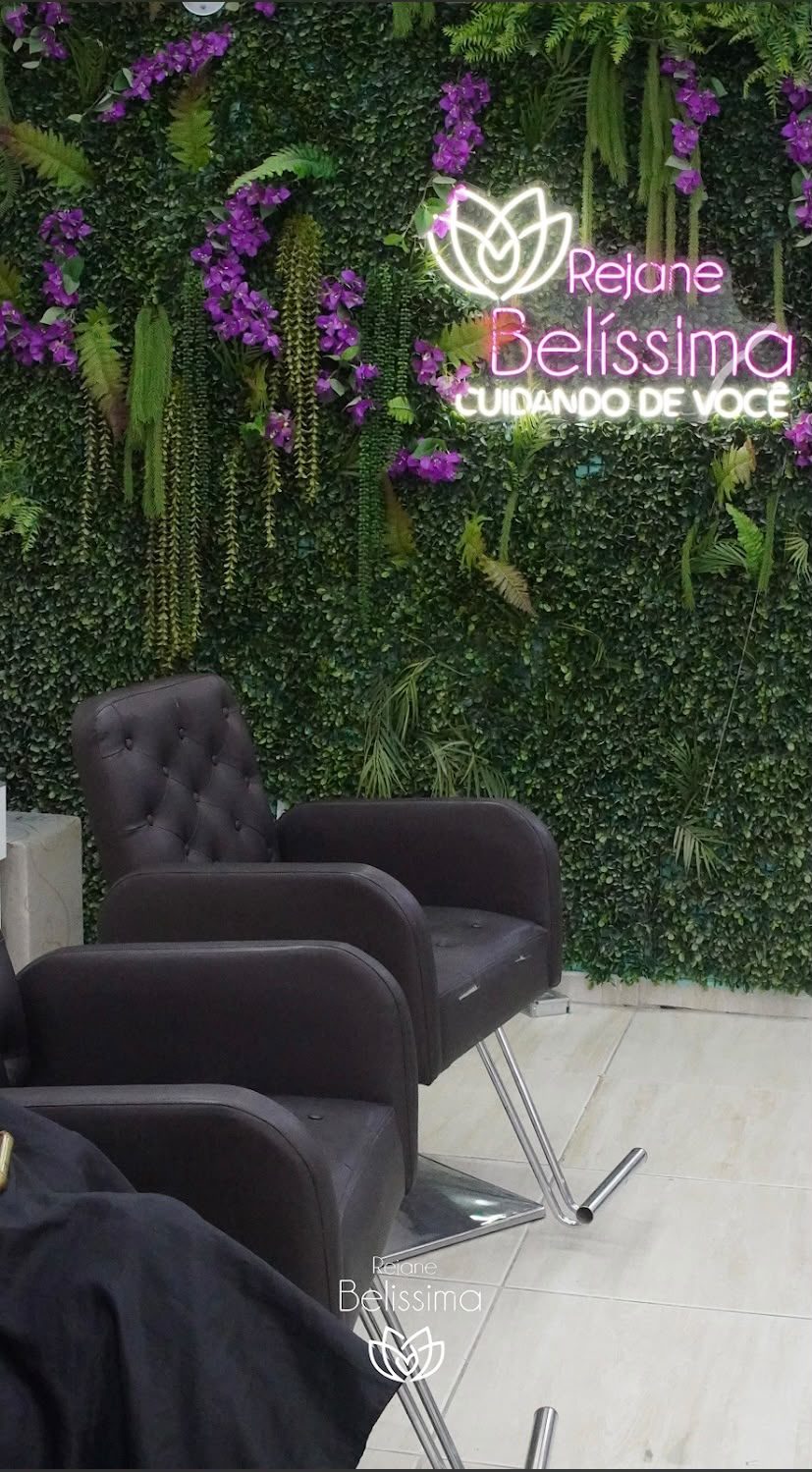 Poltronas pretas diante do painel de folhagens com o letreiro luminoso do salão